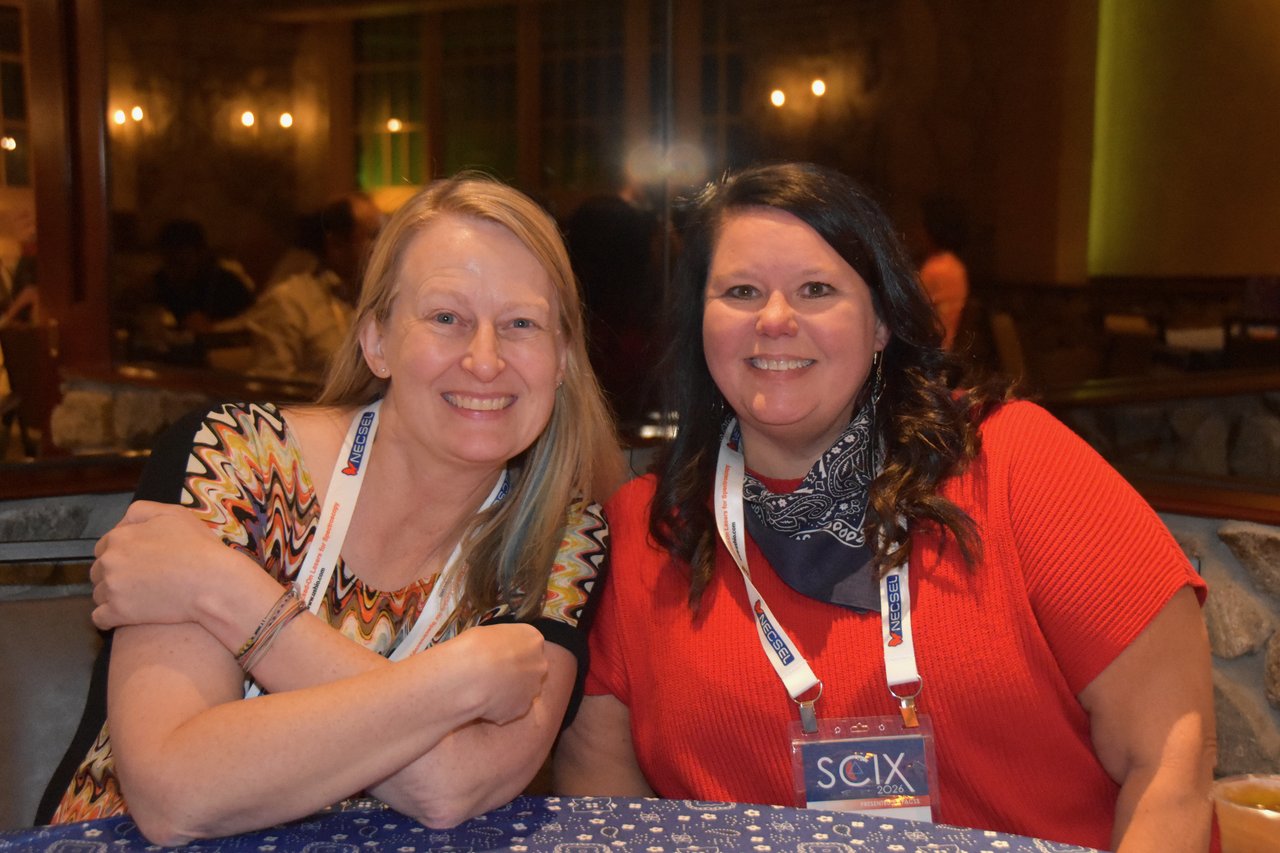 Two friends arm in arm and smiling at a SciX Gala table