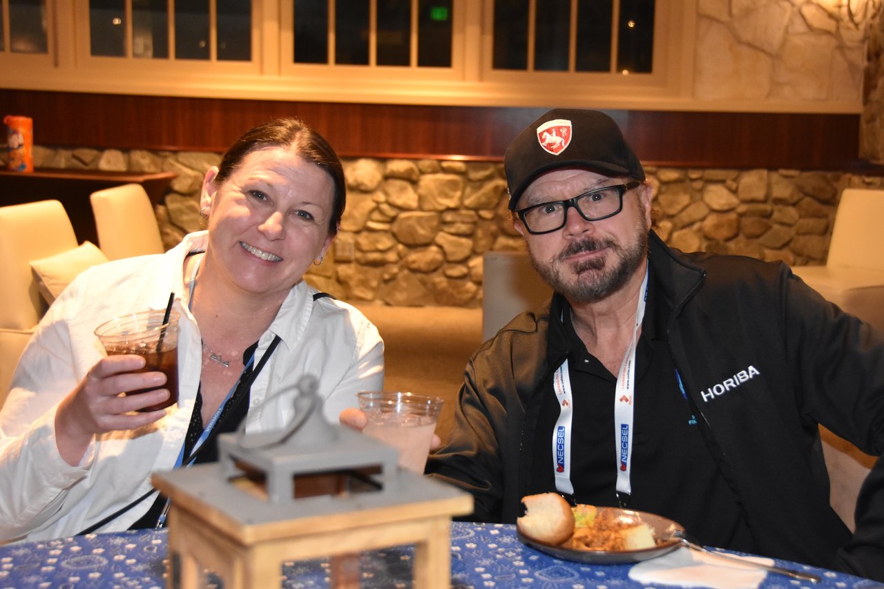 Two SciX Gala guests smiling and raising their drinks at a dinner table with a lantern centerpiece