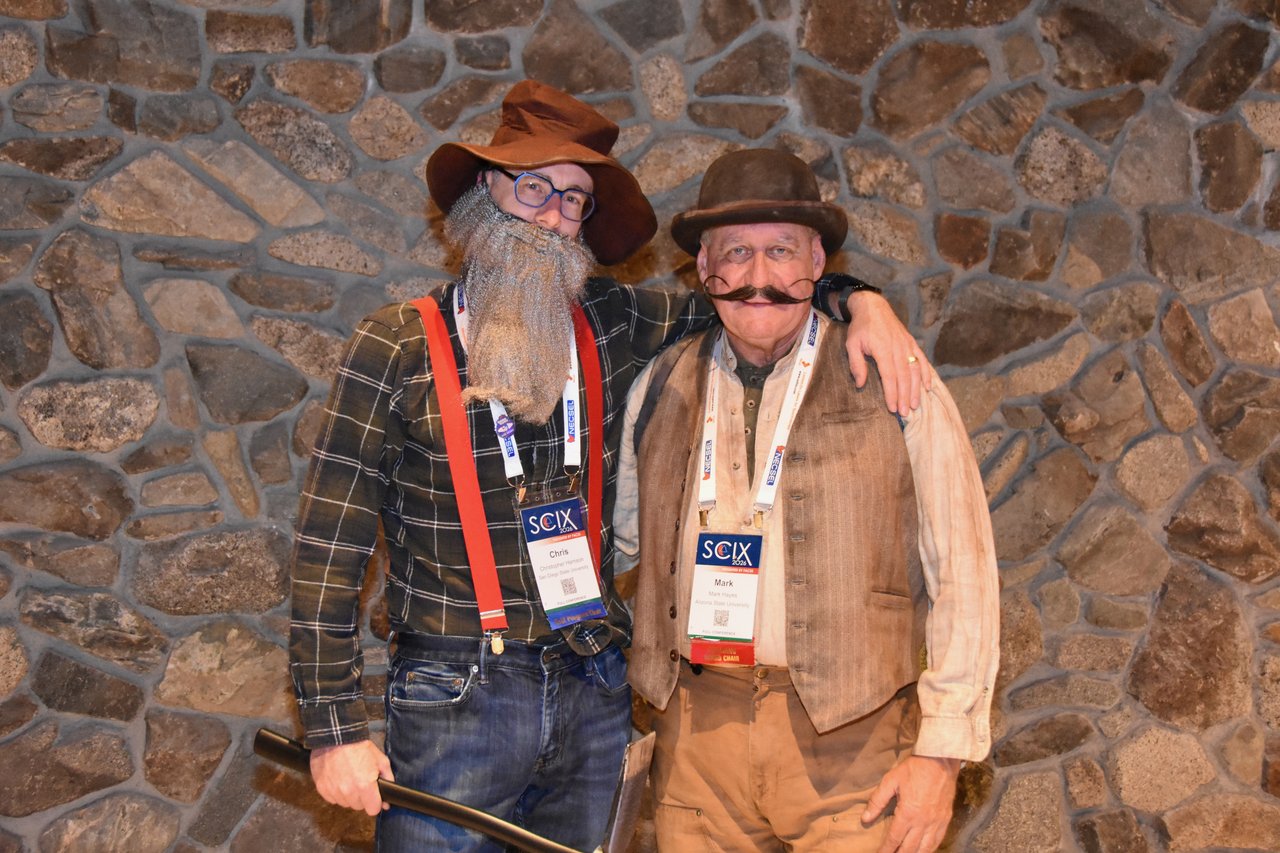 Two SciX Gala guests dressed as prospectors in front of a stone wall