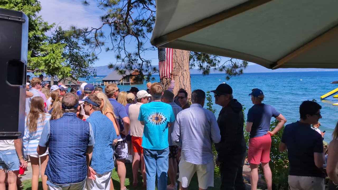 Guests standing shoulder to shoulder on the lawn, looking toward the lake