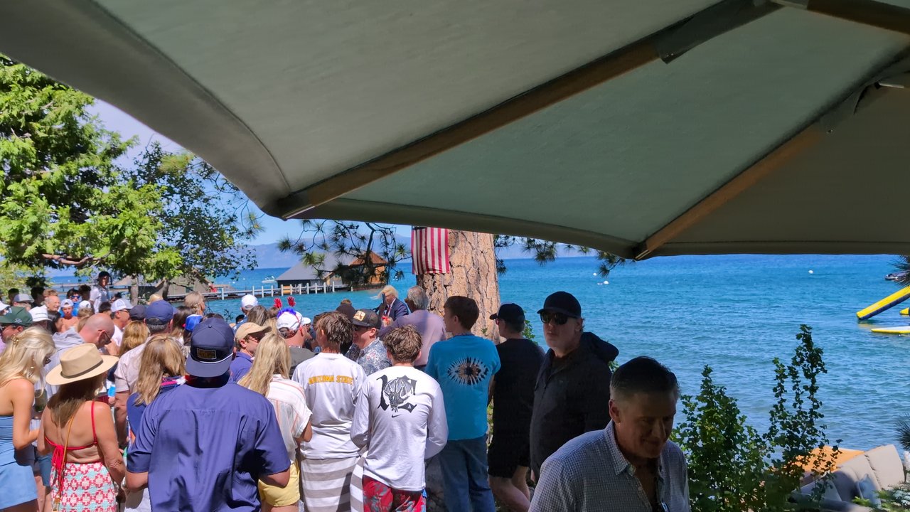A guest in a fedora turning around in the crowd by the lake
