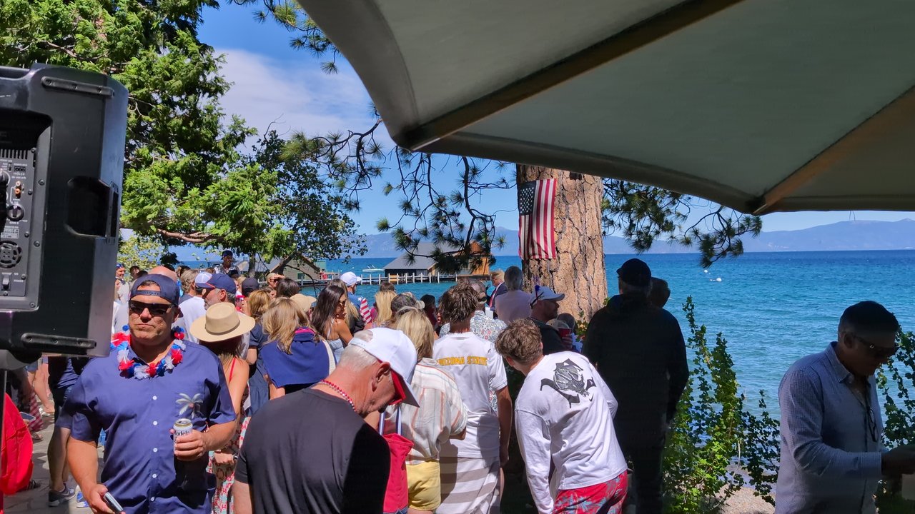 A guest in a red, white and blue lei grinning beside the DJ booth