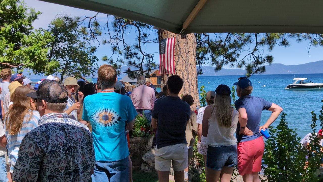 Guests gathering on the lawn by the flag on the pine, boats out on the lake