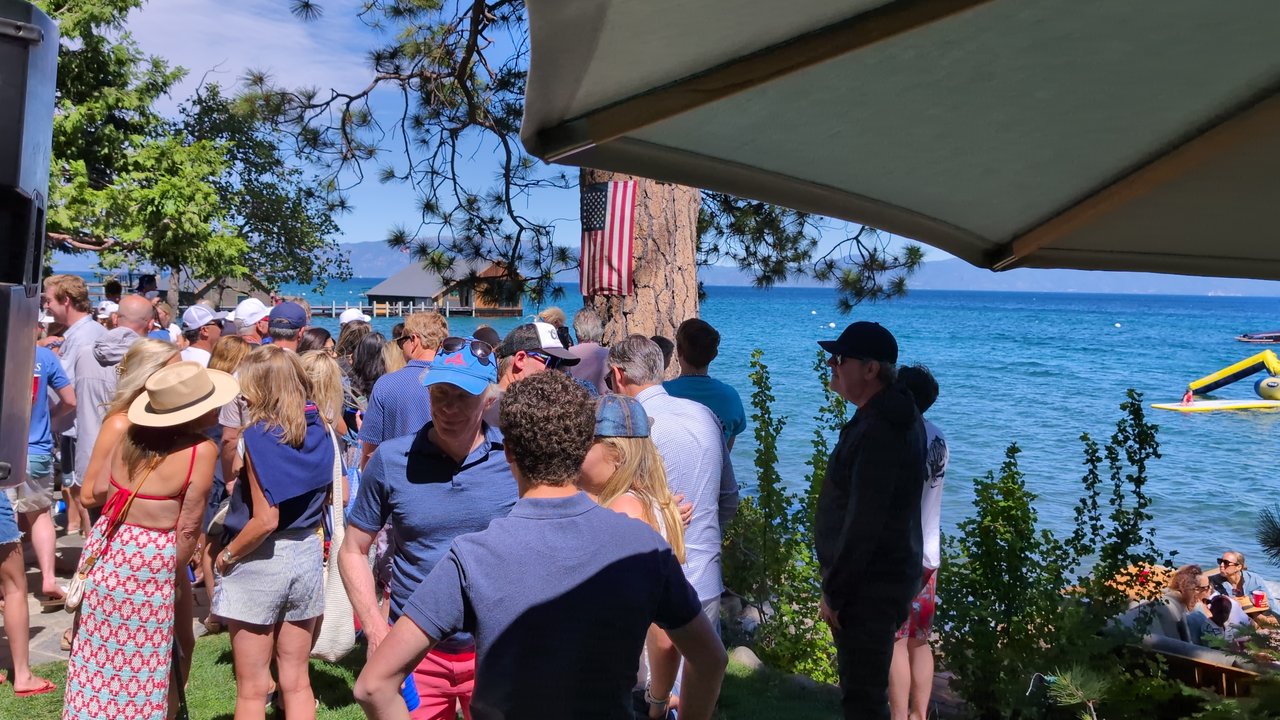 Guests in sun hats and flag shirts lined up along the lake under the pine