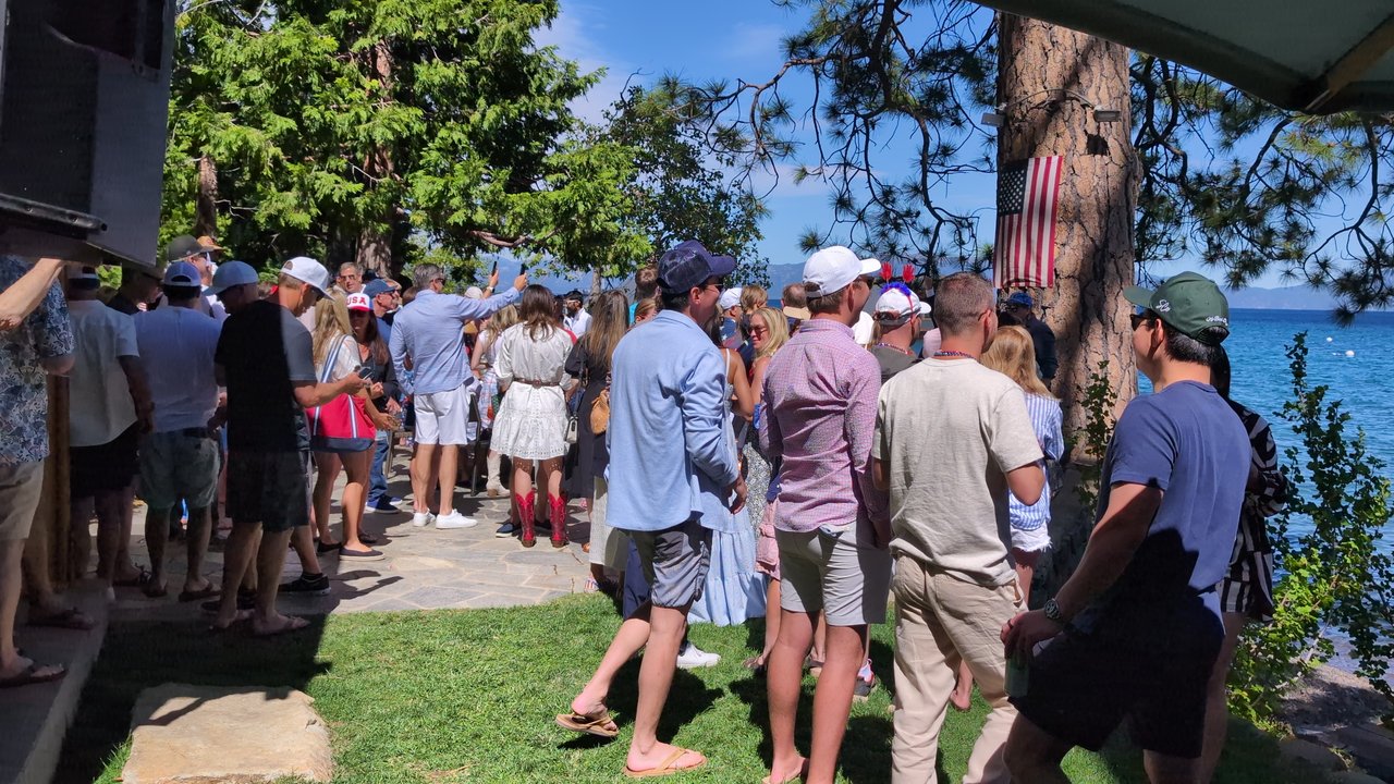 Guests filling the stone path and lawn toward the lake house