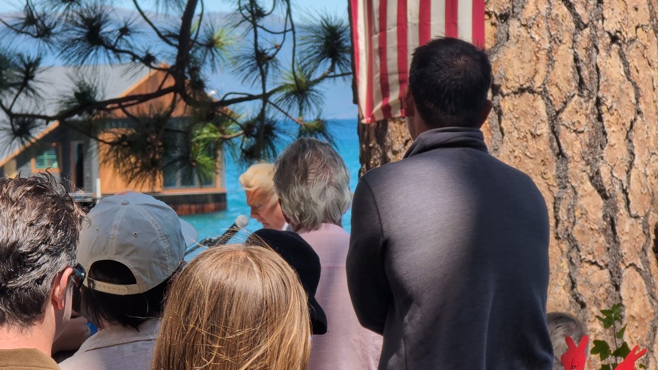 Guests gathered under the flag on the pine, a lake house across the water