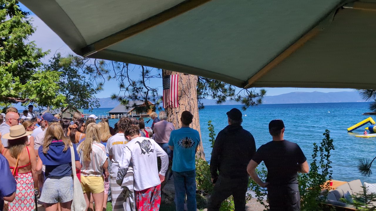Guests in white shirts and sun hats watching from the lawn above the lake