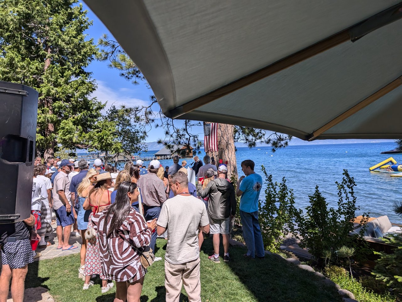 Guests crowding the lawn by the lake under the patio umbrella