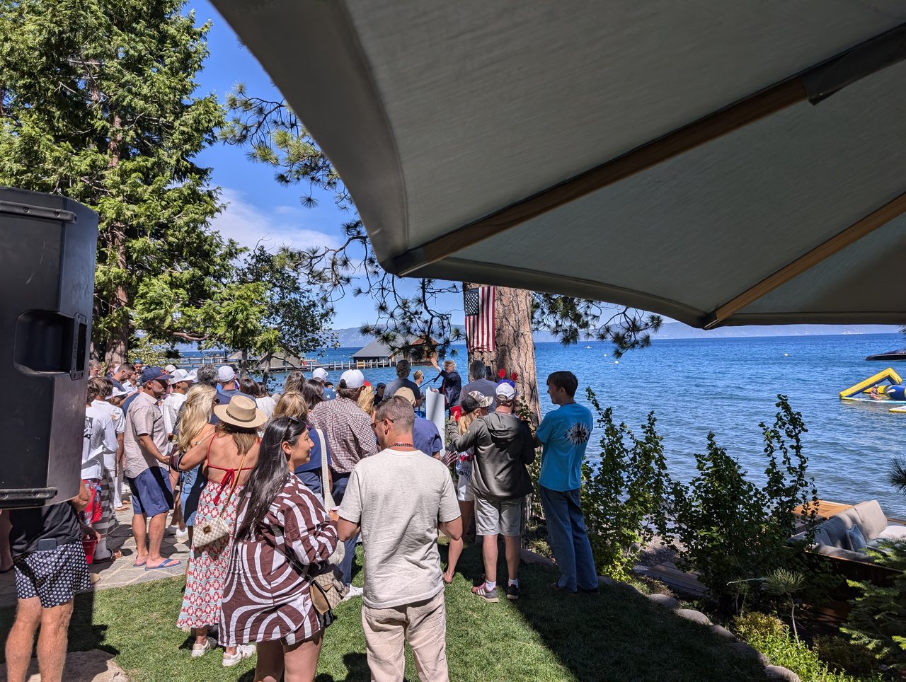 Guests in sun hats on the grass beside the speaker, the lake behind