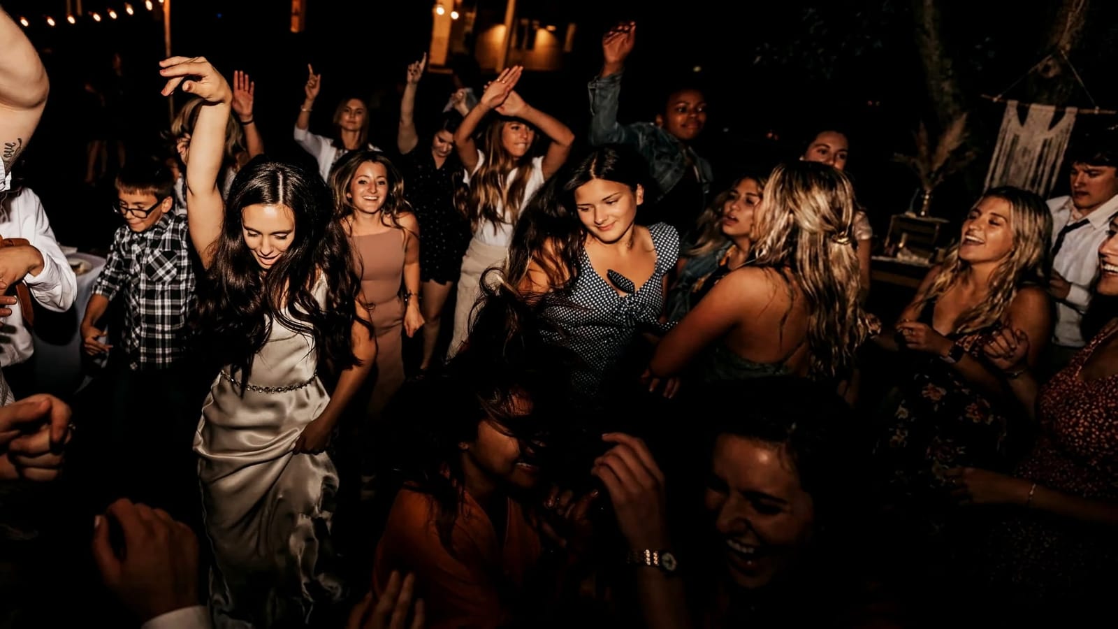 A packed dance floor at Lindsey and Nathanael's reception at Twenty Mile House, with Lindsey dancing in her satin dress among her friends under the string lights