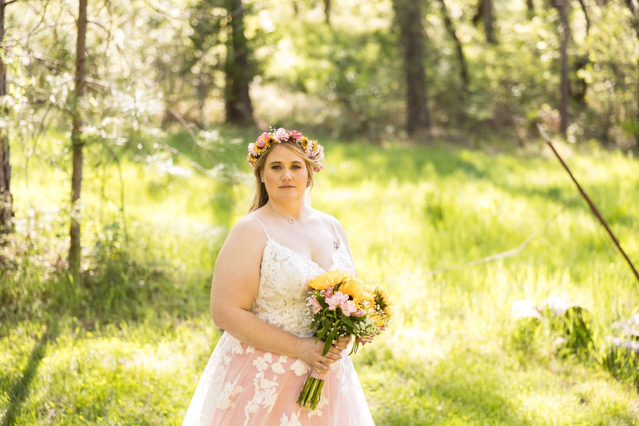 Abney stands alone in a sunlit meadow holding her bouquet