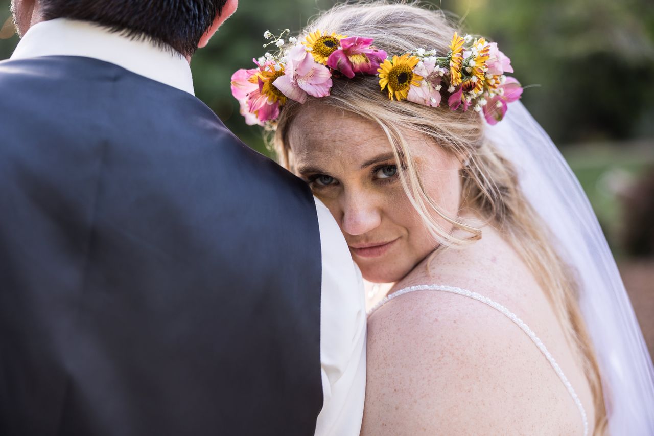Abney looks at the camera over Chris's shoulder, wearing her crown of sunflowers and pink flowers