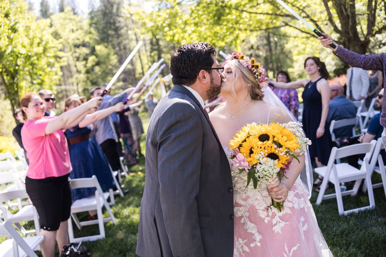 Abney and Chris kiss in the aisle while their guests hold lightsabers overhead