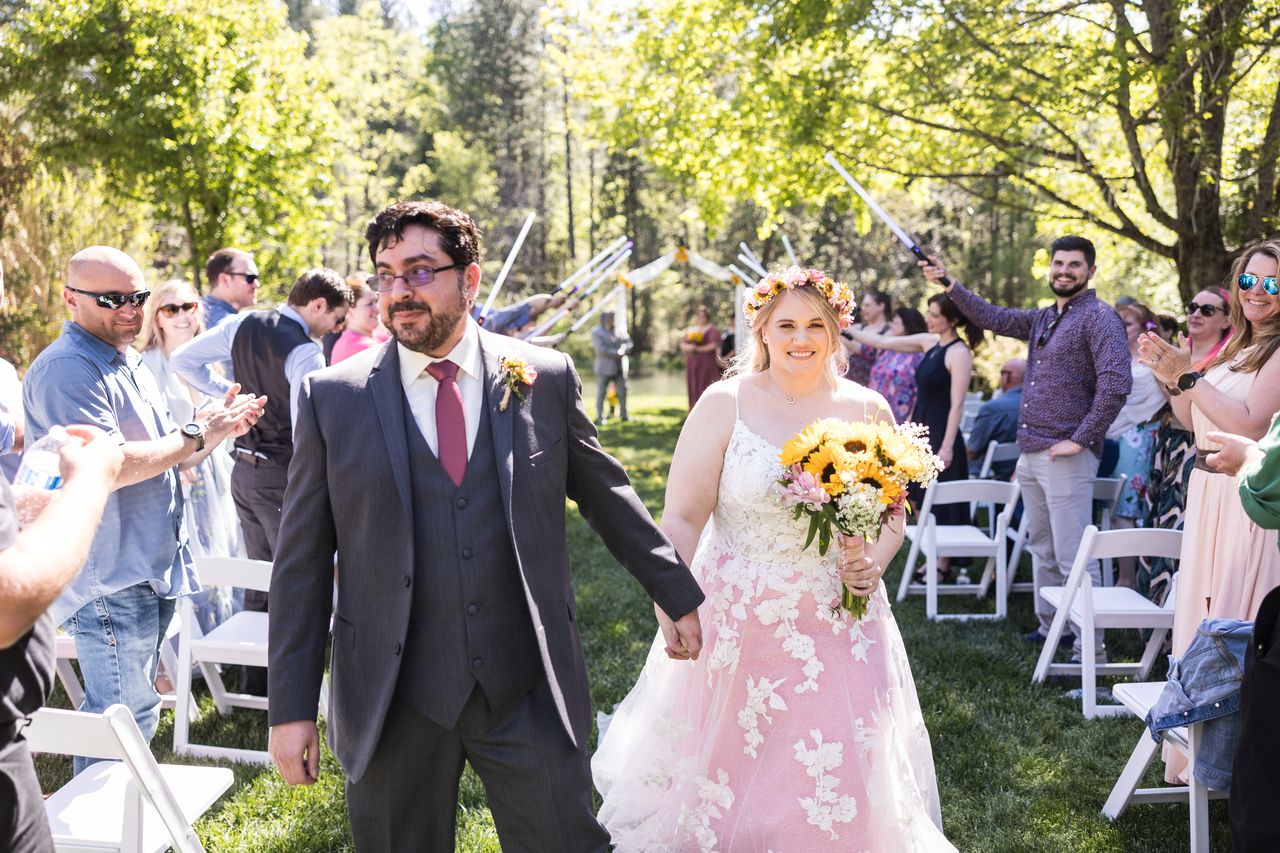 Chris grins as he and Abney walk up the aisle beneath their guests' lightsabers