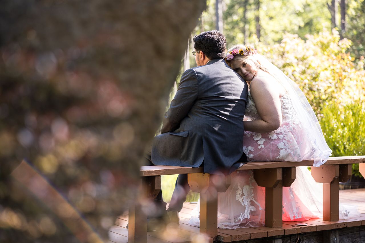 Abney and Chris sit together on a bench, seen through the branches of a tree