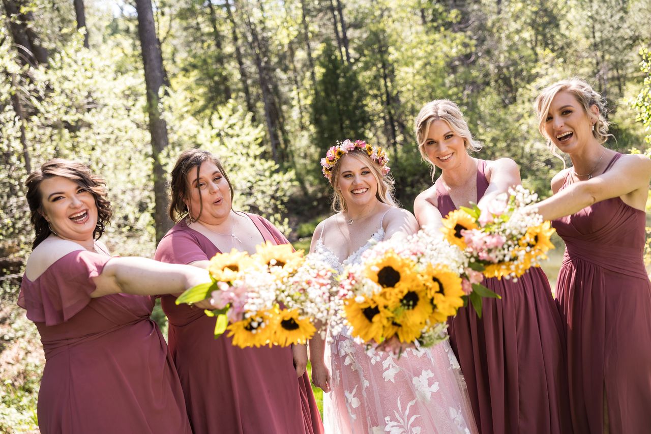 Abney and her bridesmaids laugh as they hold their bouquets out toward the camera