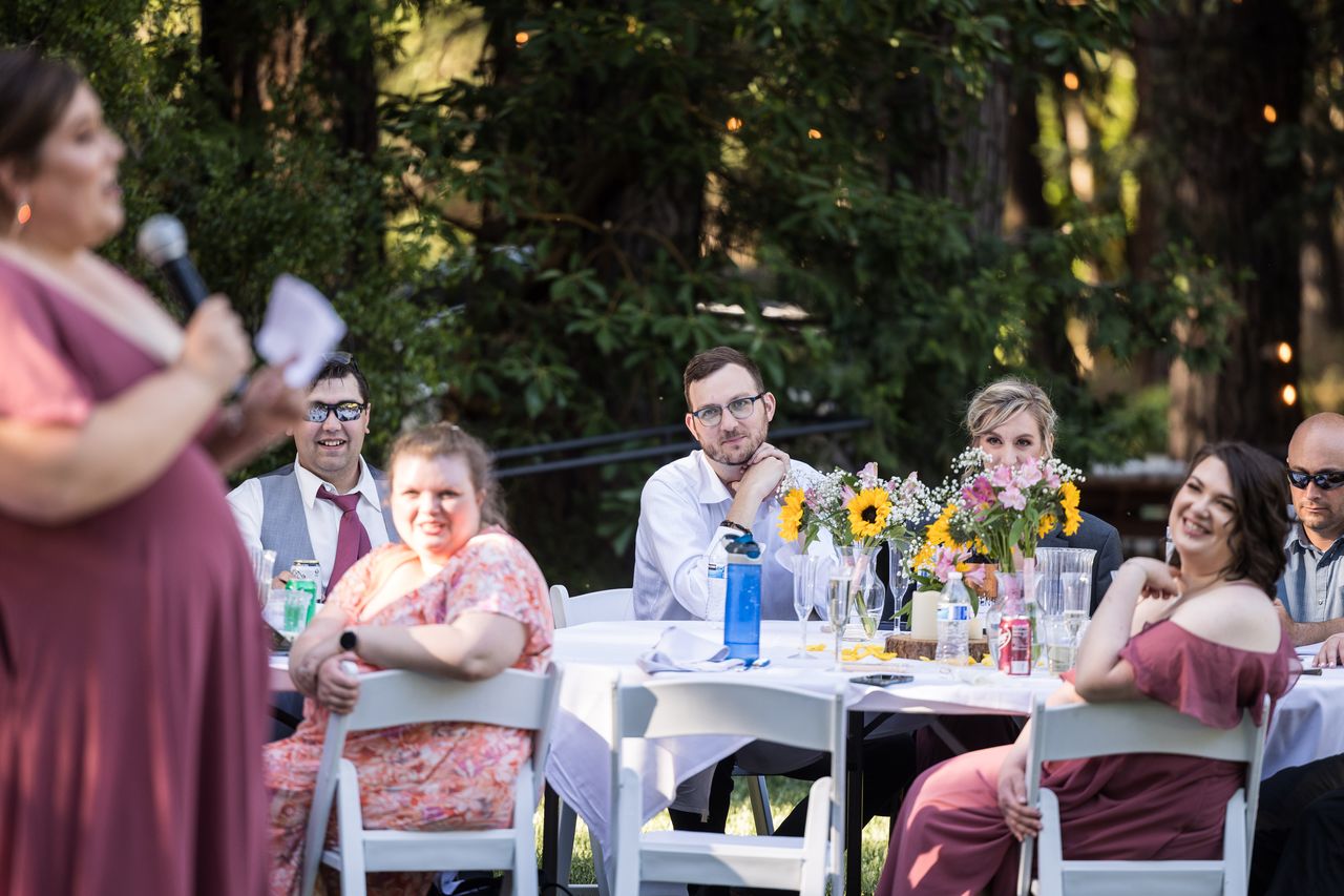 A bridesmaid gives her toast with a microphone as seated guests smile