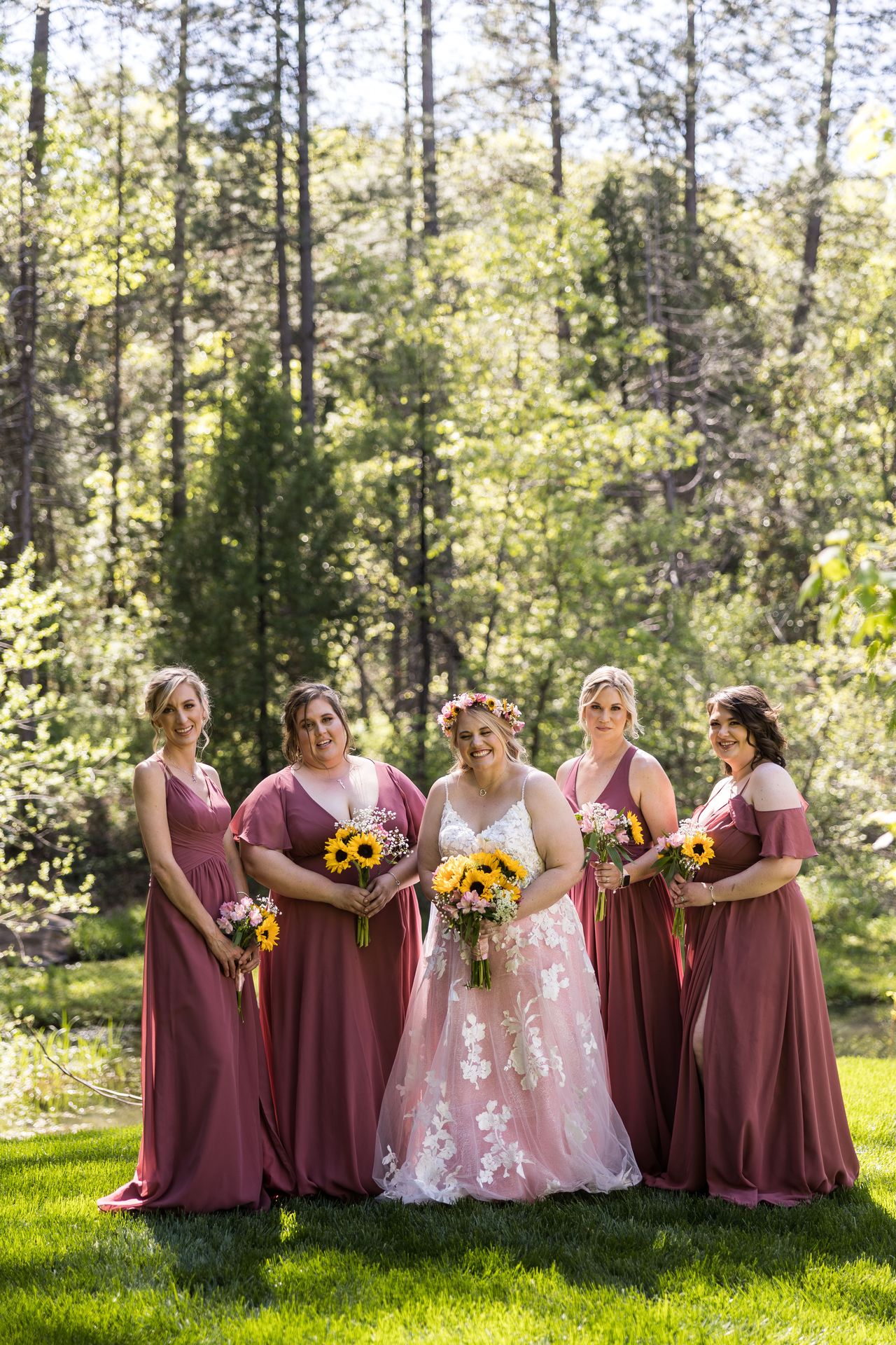Abney and her bridesmaids stand together on the lawn beneath tall pines