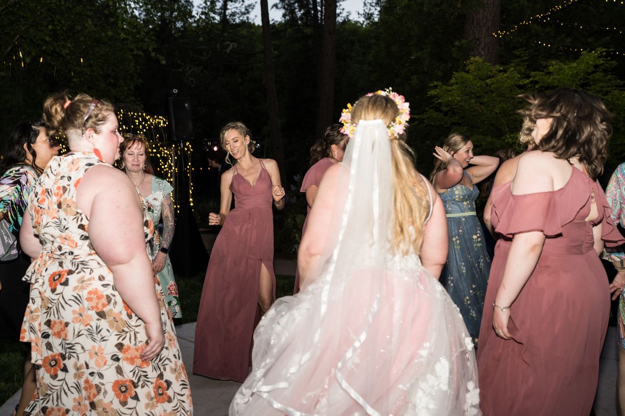 Abney, seen from behind in her veil and flower crown, dances in a circle of bridesmaids and guests