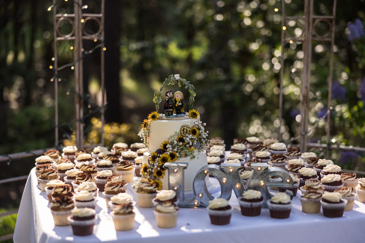 The dessert table with the wedding cake and rows of cupcakes in the evening shade