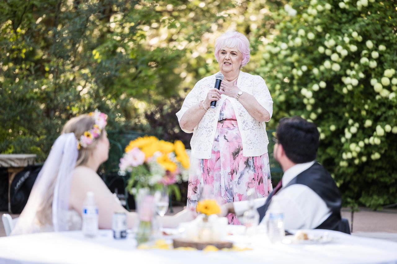 A family member in a pink floral dress gives a toast while Abney and Chris watch