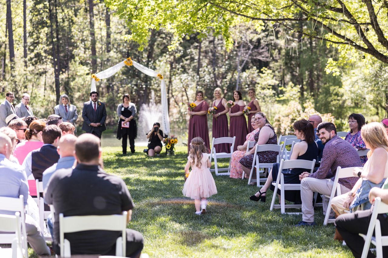 The flower girl walks down the grass aisle while guests turn to watch