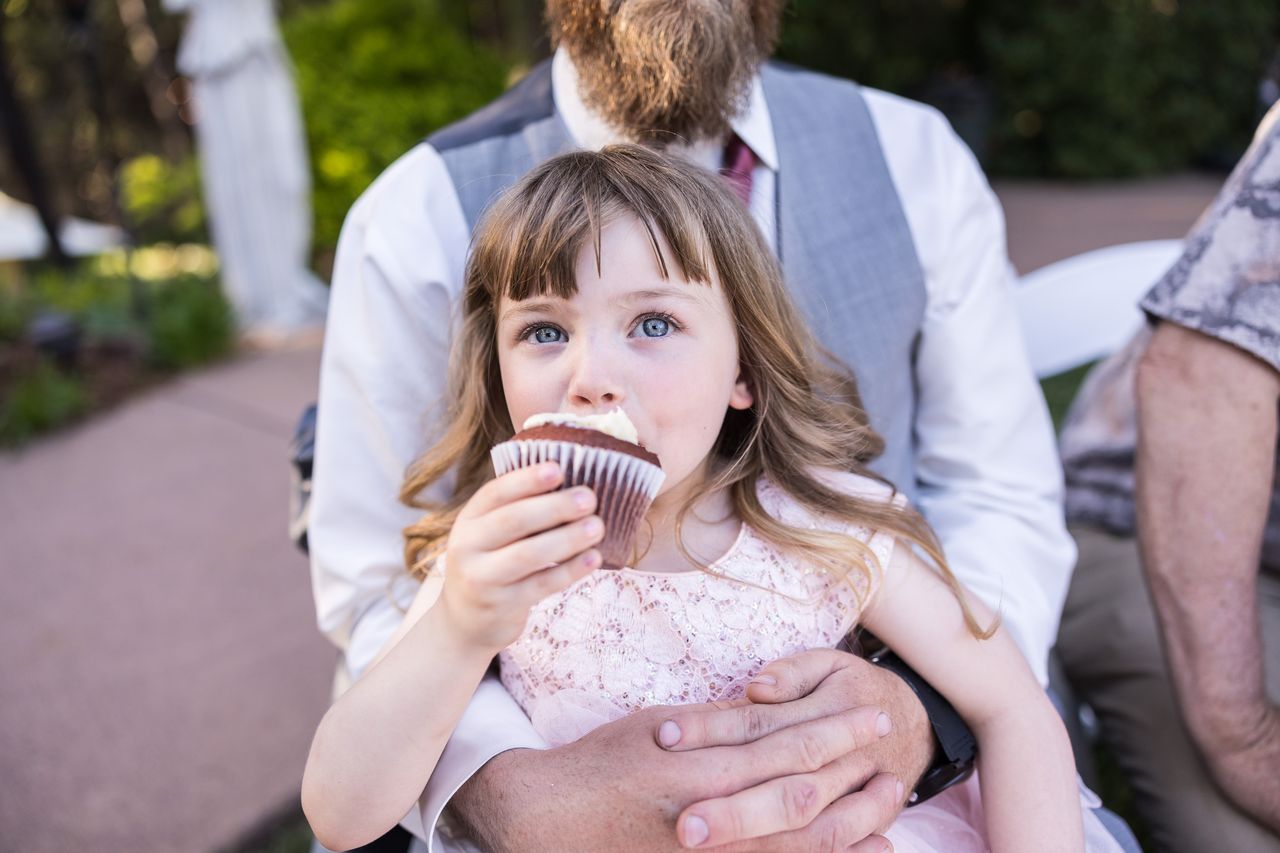 The flower girl takes a bite of a chocolate cupcake