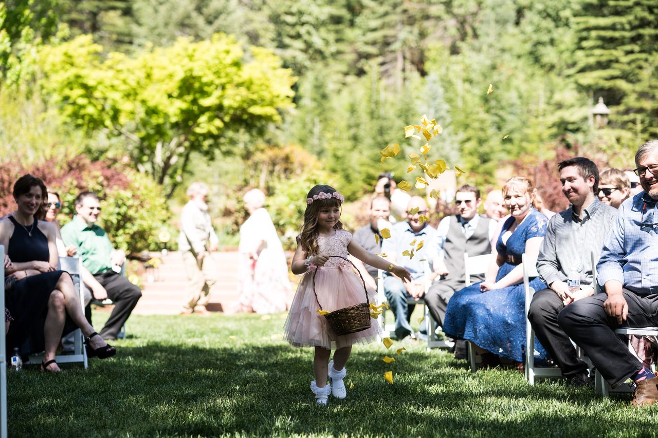 The flower girl scatters petals as she walks past seated guests