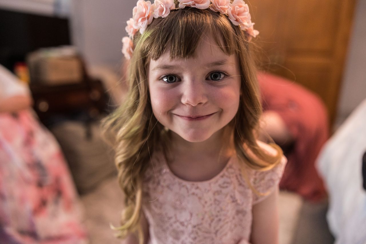 The flower girl smiles up at the camera in her pink flower crown