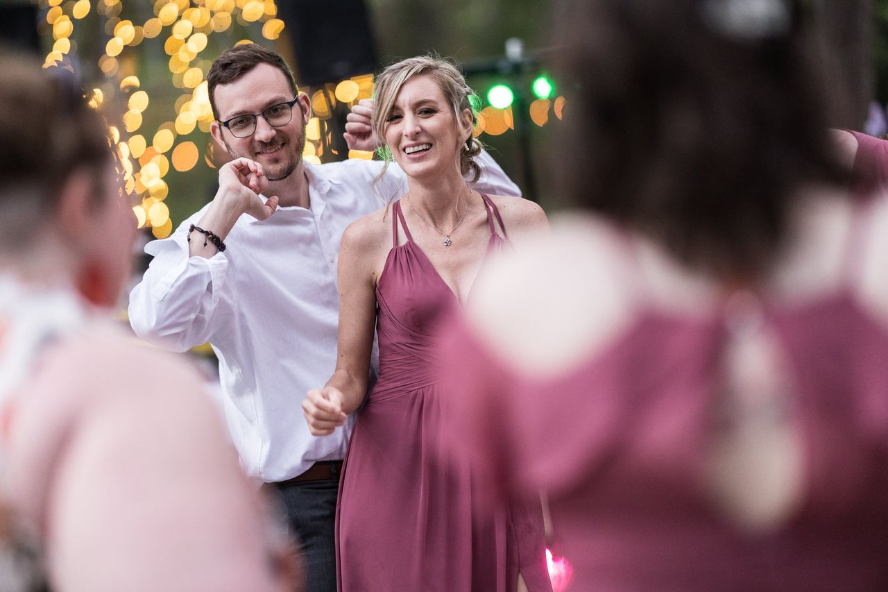 Two guests smile and dance together in front of glowing string lights
