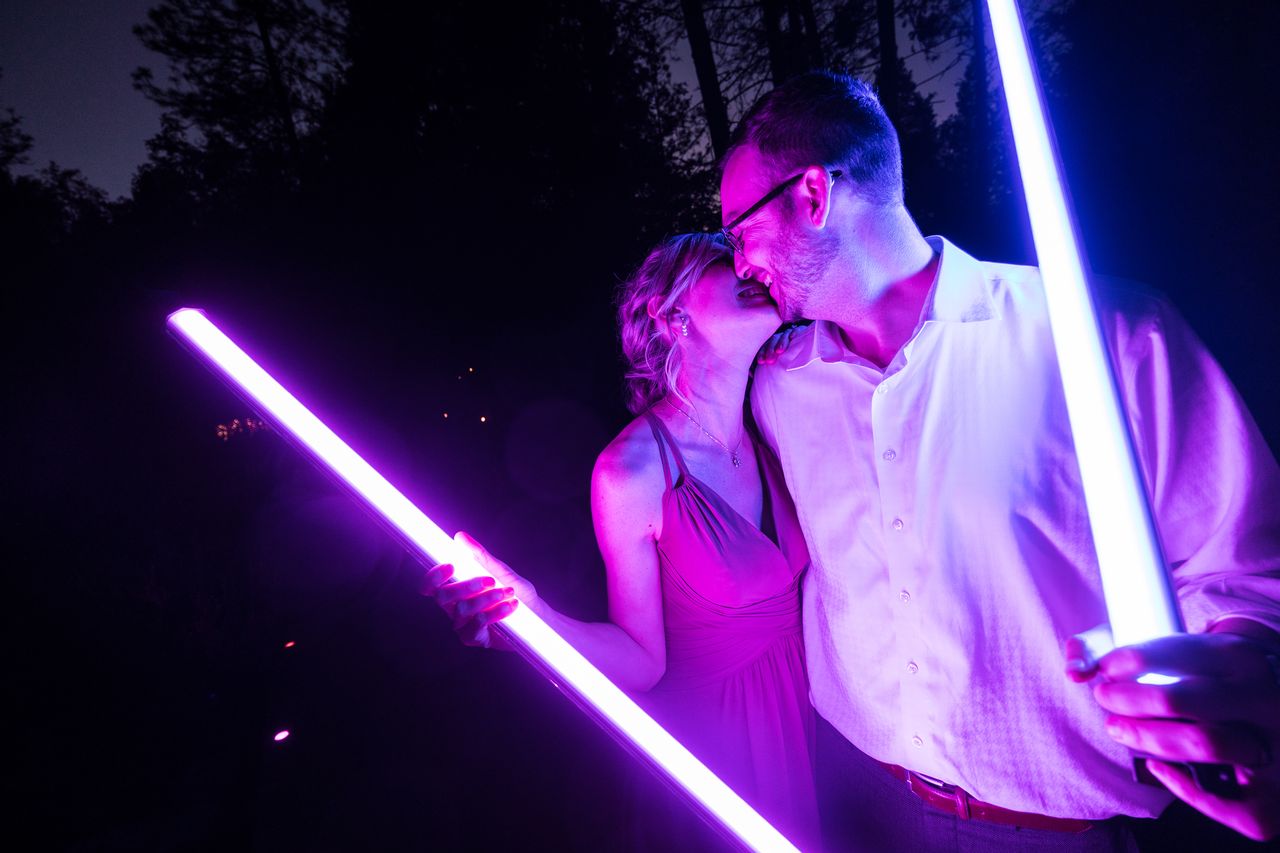 Two wedding guests share a kiss while each holds a glowing lightsaber