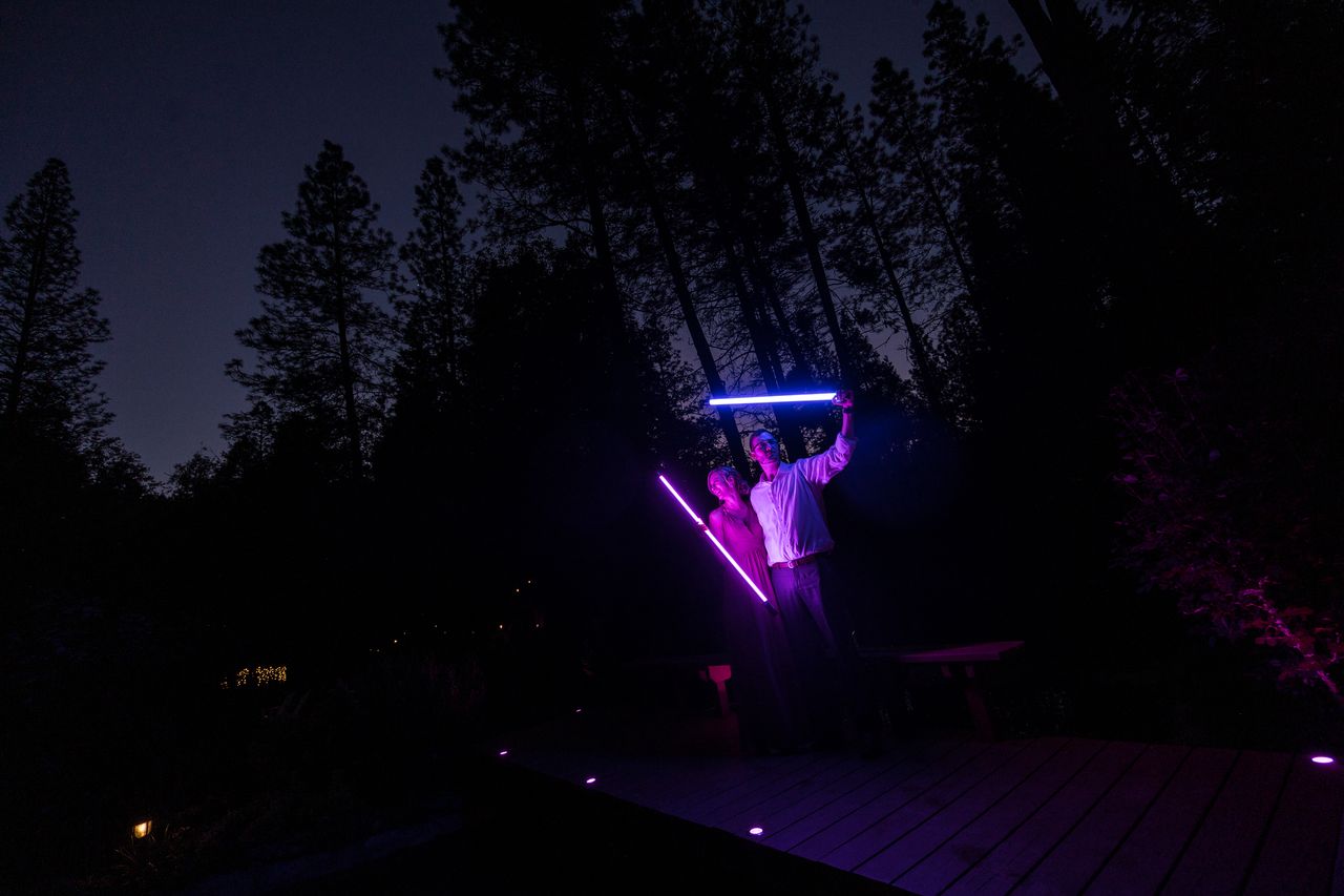 Two guests raise glowing lightsabers on the dock in the dark