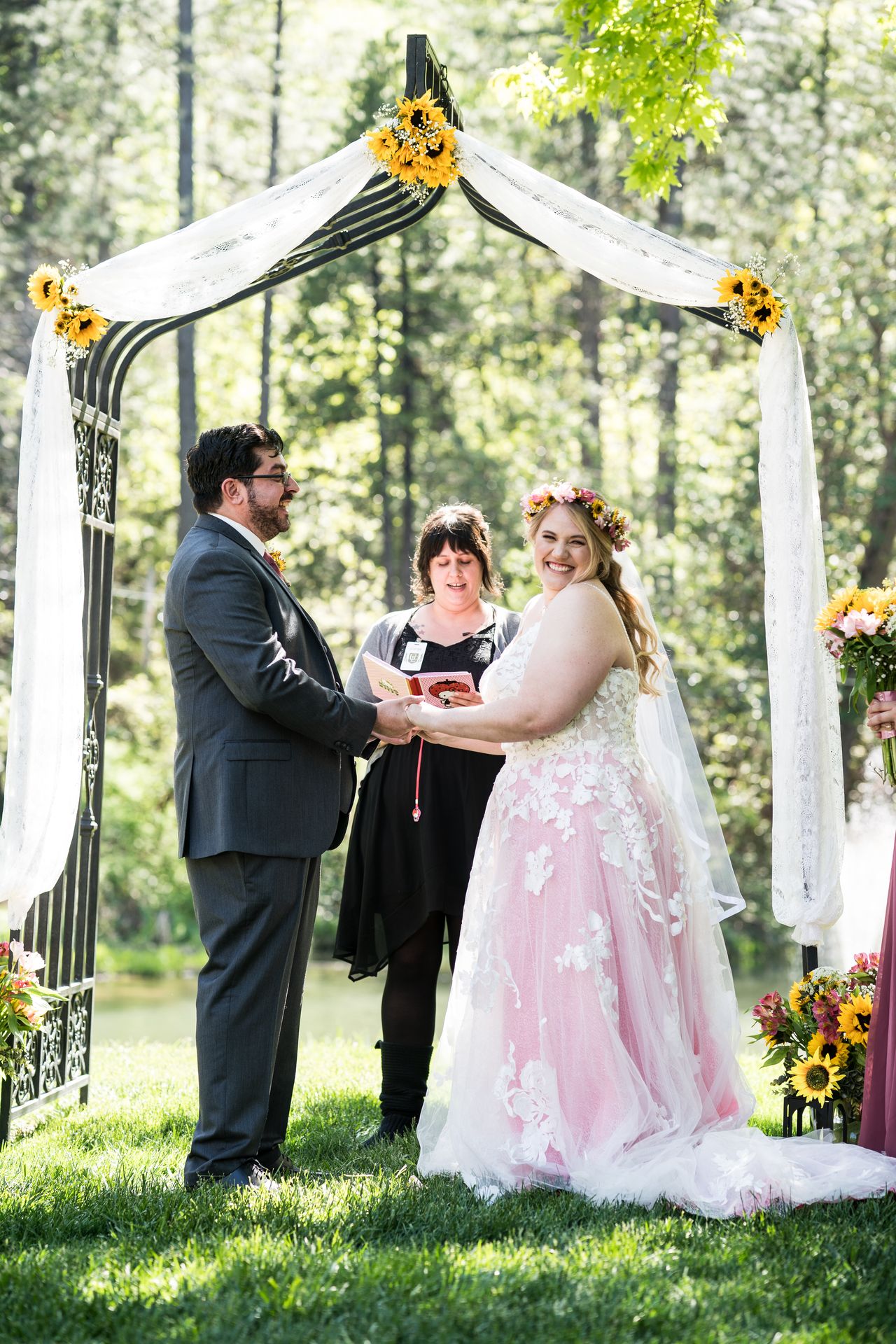 Abney and Chris hold hands under the arbor with the pond behind them