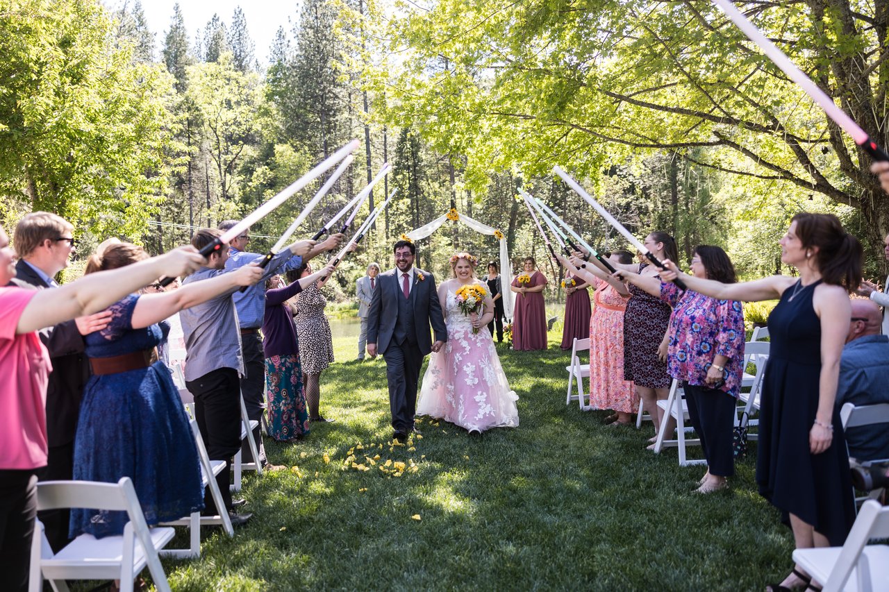 Abney and Chris walk back up the aisle under an arch of lightsabers held by their guests