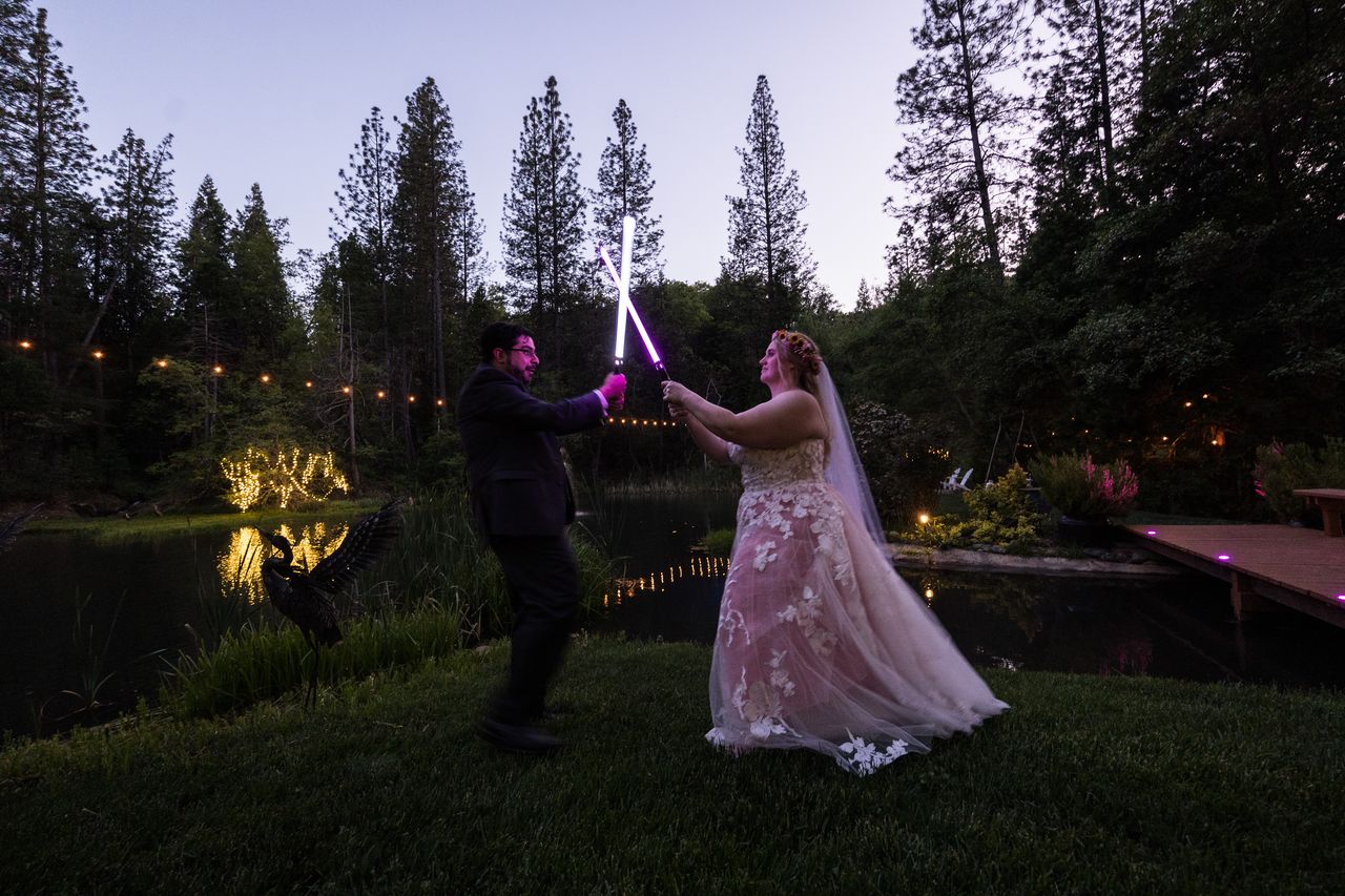 Abney and Chris cross lightsabers above their heads beside the pond