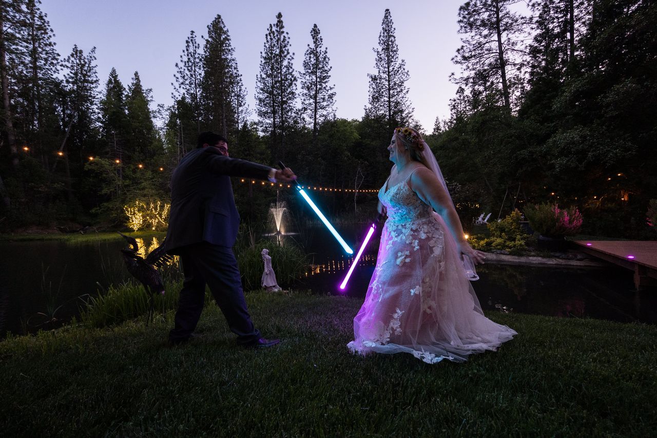 Chris swings a blue lightsaber toward Abney's purple one as they duel beside the pond