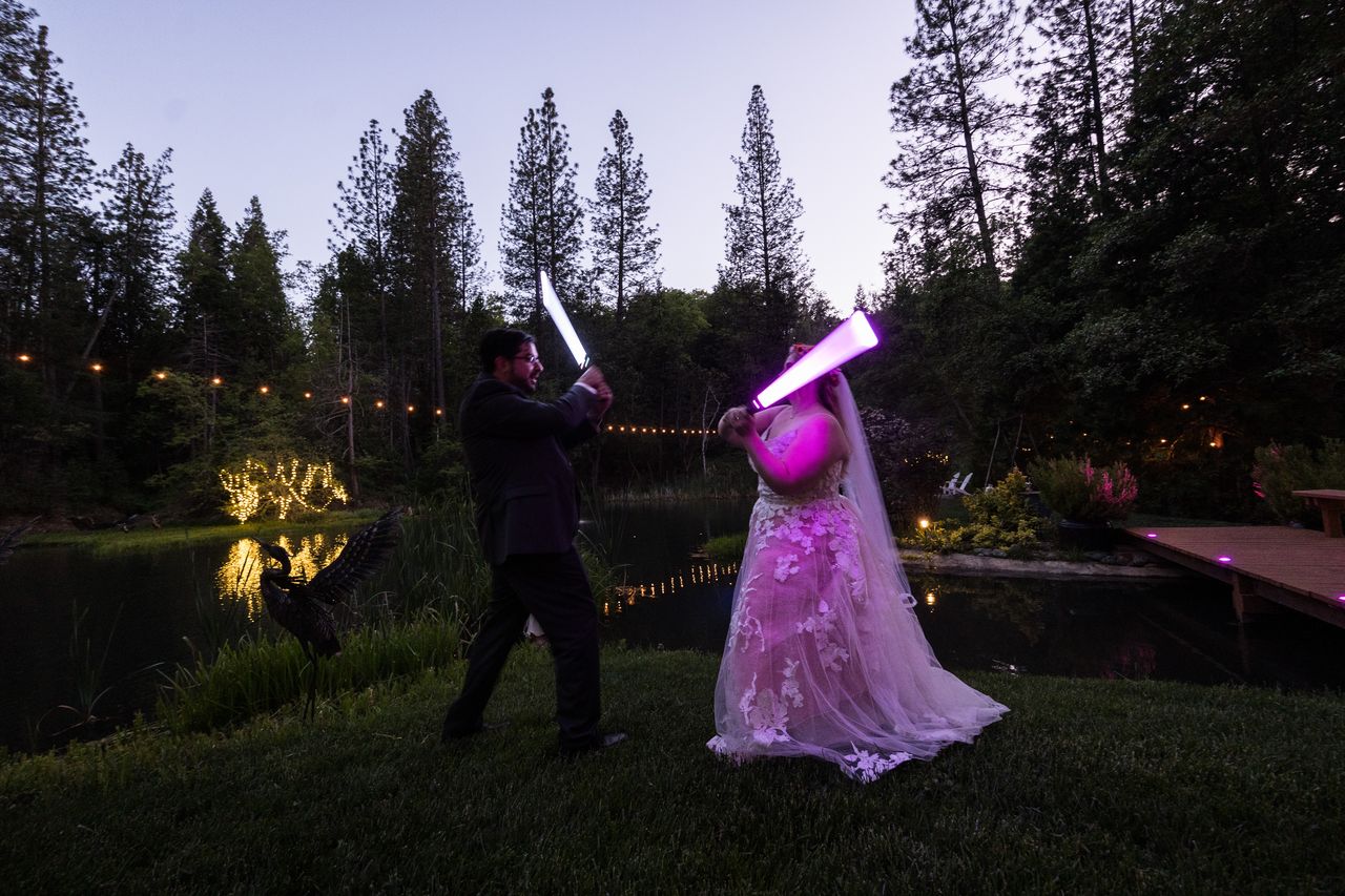 Chris and Abney swing their lightsabers toward each other beside the pond