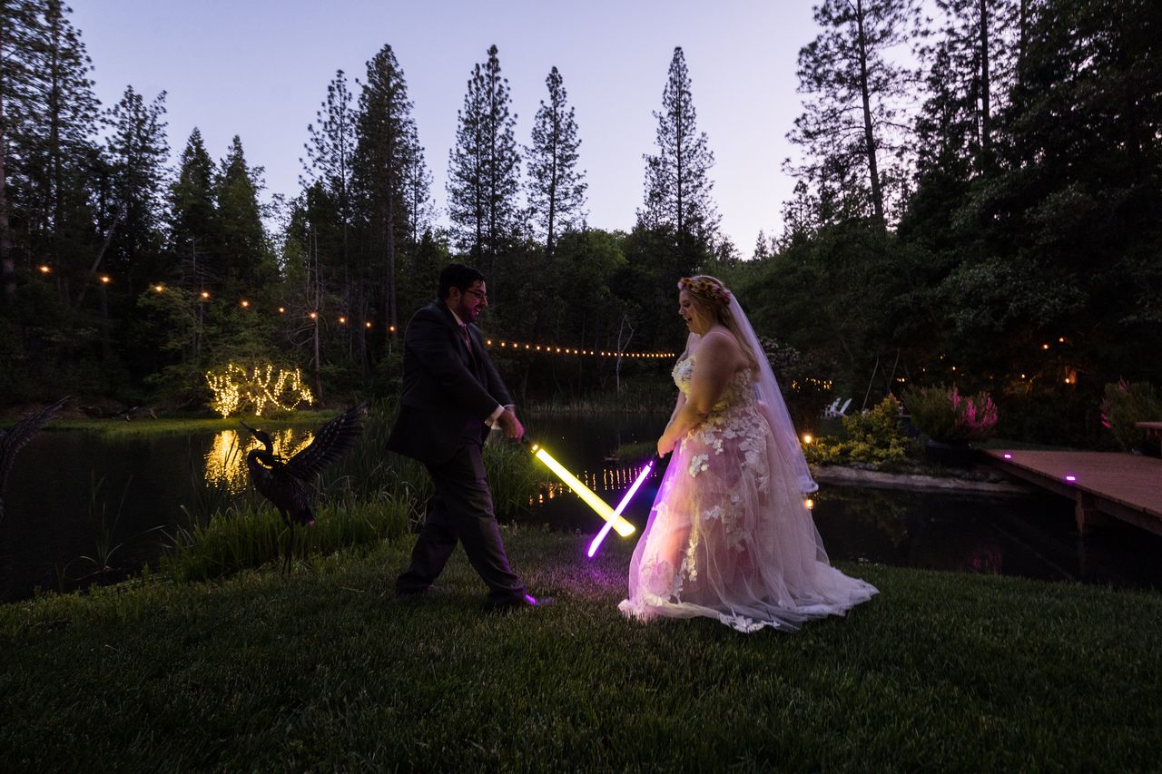 Chris and Abney lower a yellow lightsaber and a purple one toward the grass beside the pond
