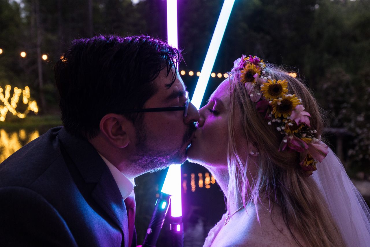 Abney and Chris kiss in front of two glowing lightsabers