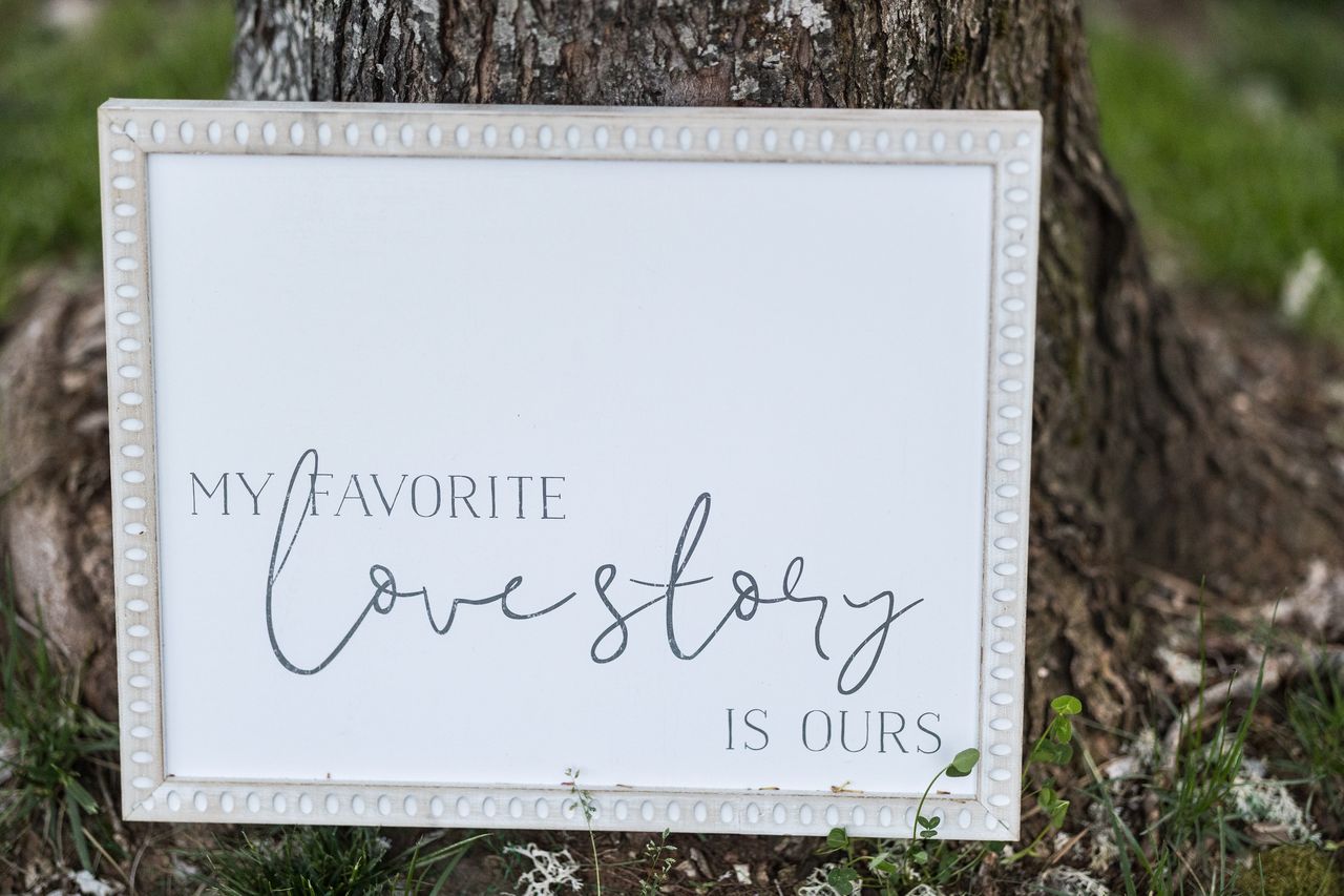 A framed sign reading My favorite love story is ours, leaning against the tree beside the photo booth