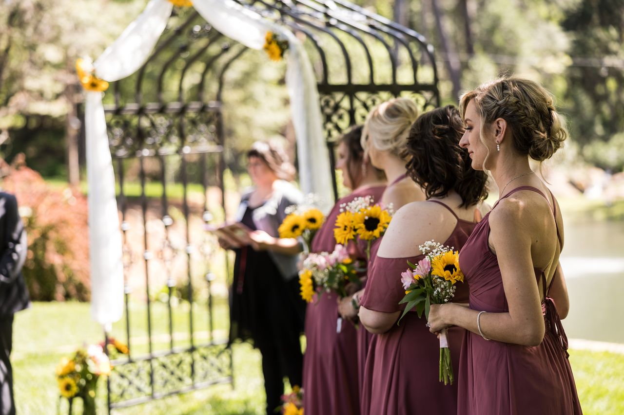 The officiant and bridesmaids stand at the sunflower arbor