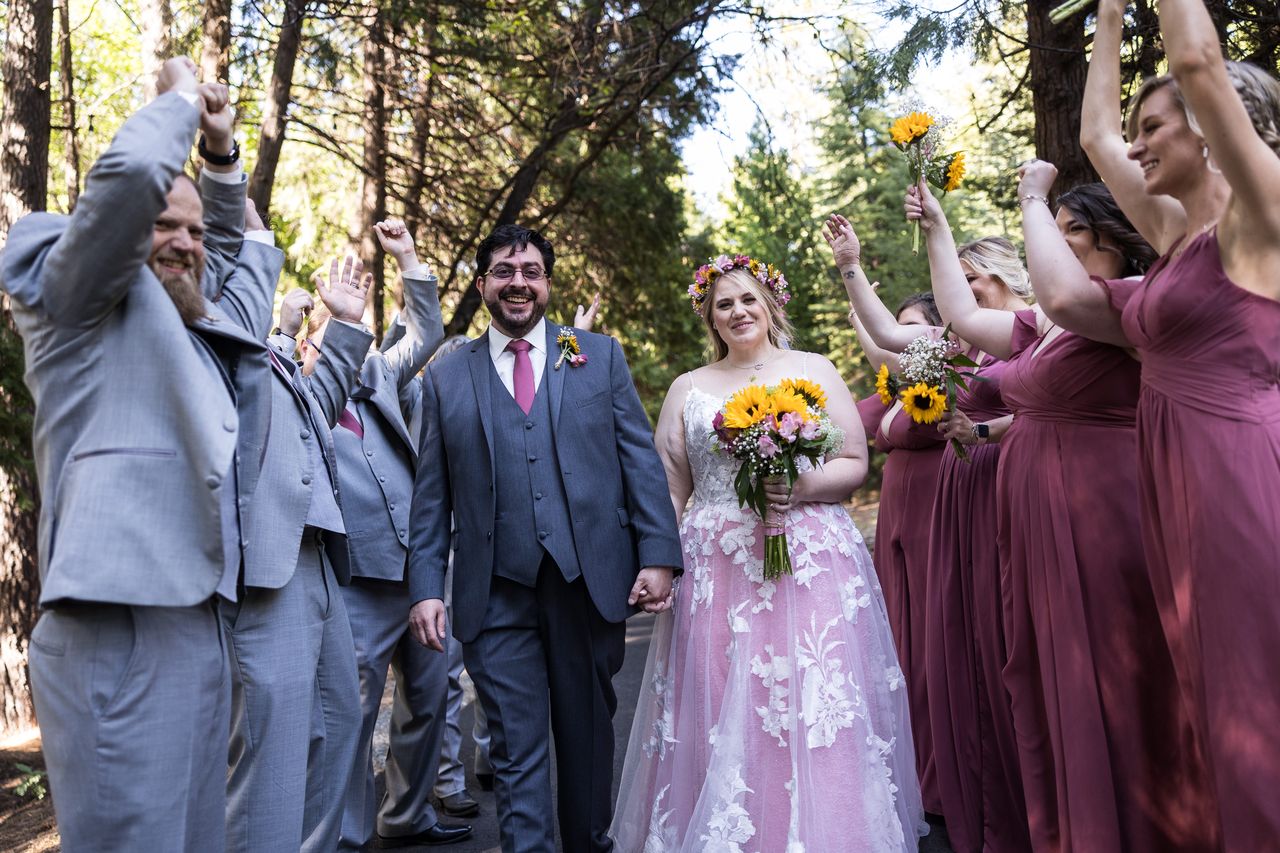 The wedding party cheers around Abney and Chris as they walk down a forest path