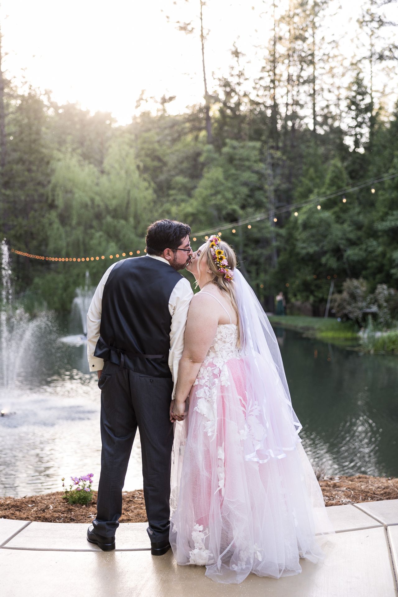 Abney and Chris kiss at the edge of the pond, with string lights and a fountain behind them