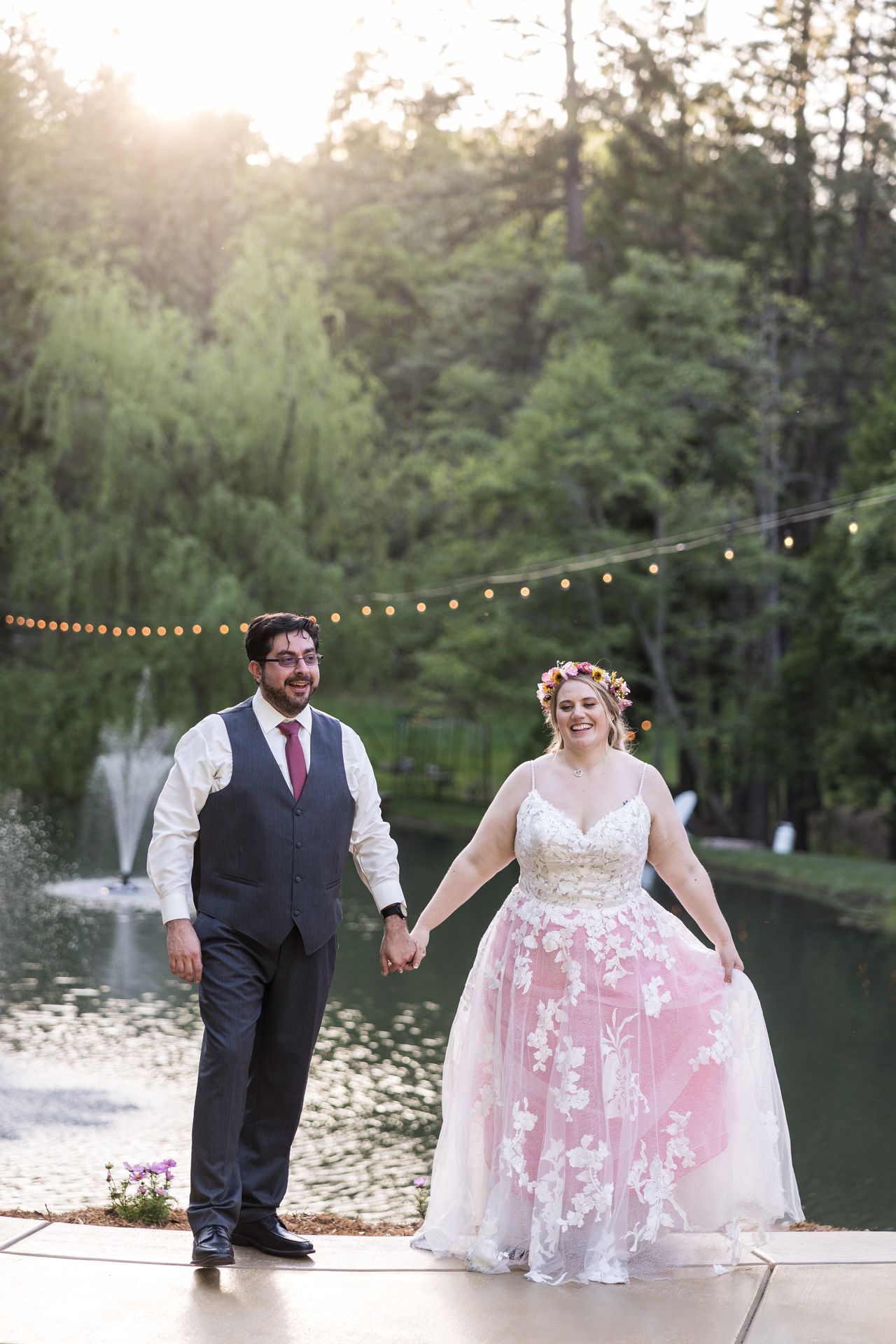 Abney and Chris hold hands and laugh as they walk along the pond at sunset