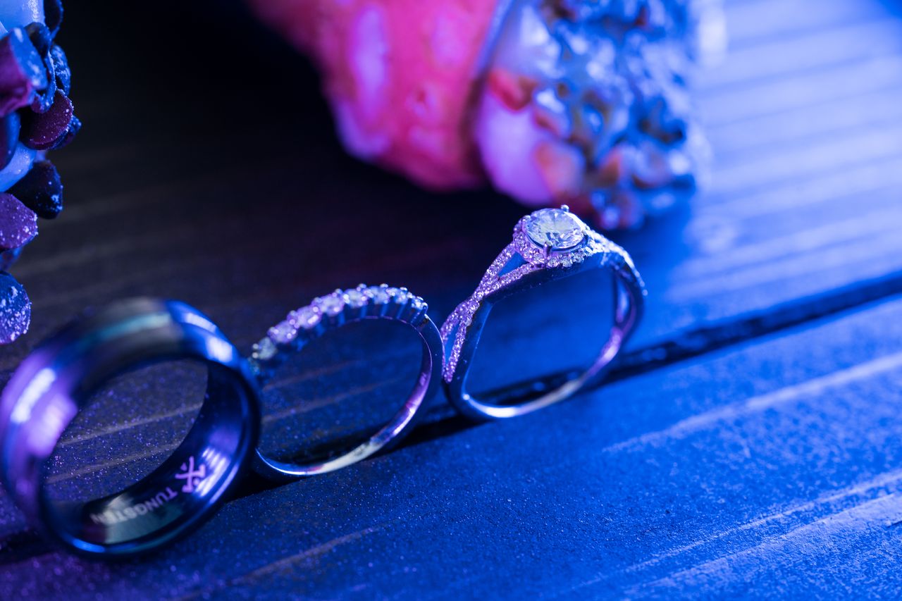 The three wedding rings standing in a row on a wooden board, lit in blue and purple