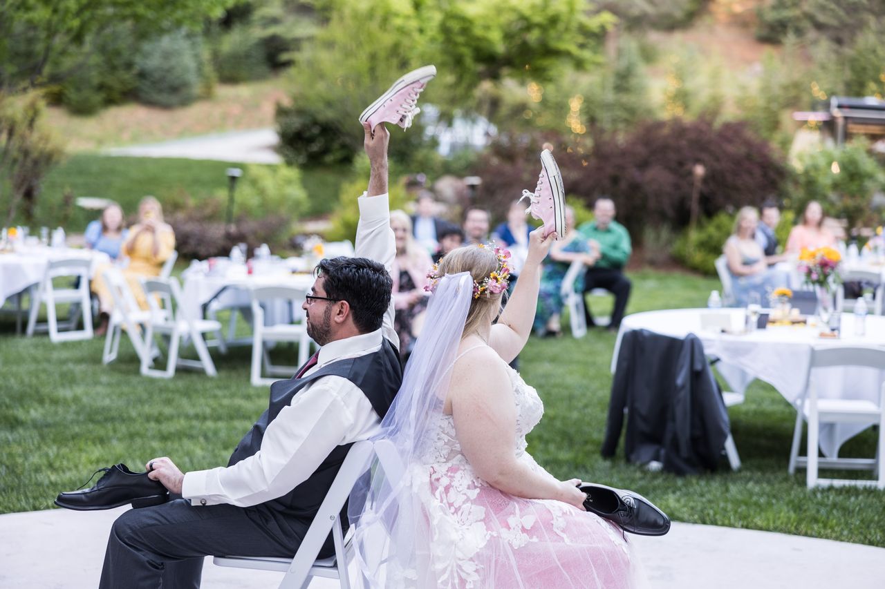 Abney and Chris sit back to back for the shoe game, each holding up a pink sneaker while guests watch from their tables