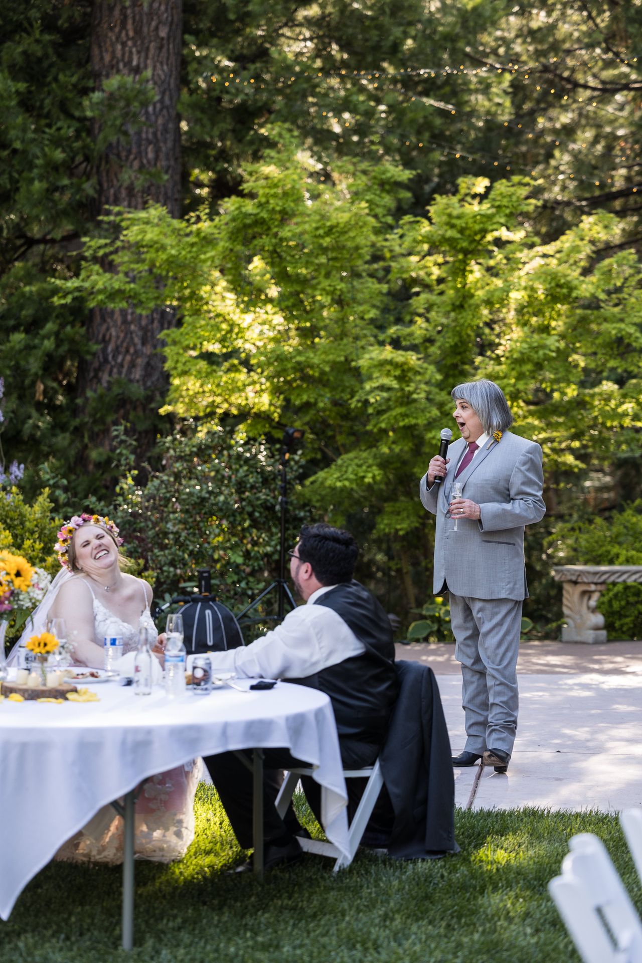 A family member gives a toast with a microphone while Abney and Chris listen from their table
