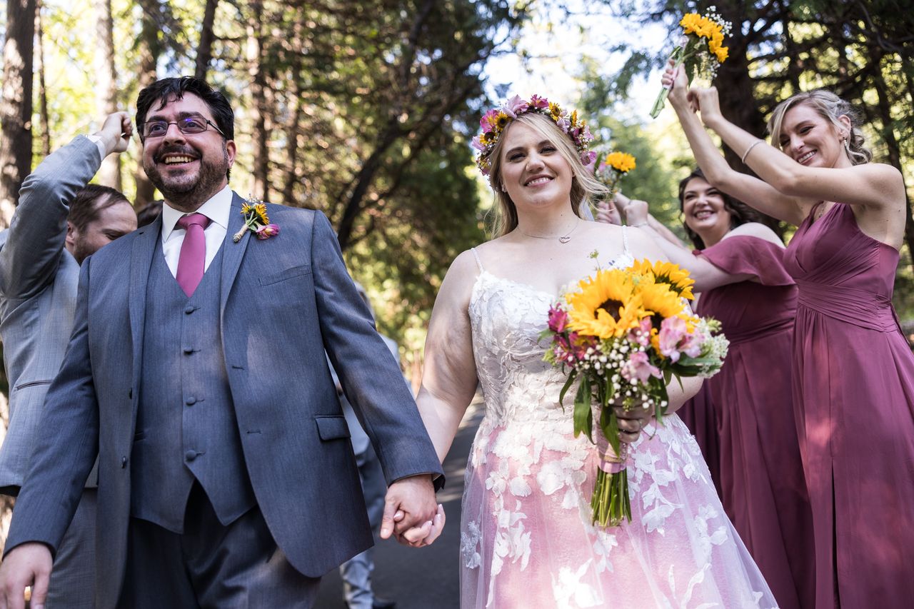 Abney and Chris walk hand in hand, laughing, as their wedding party celebrates behind them