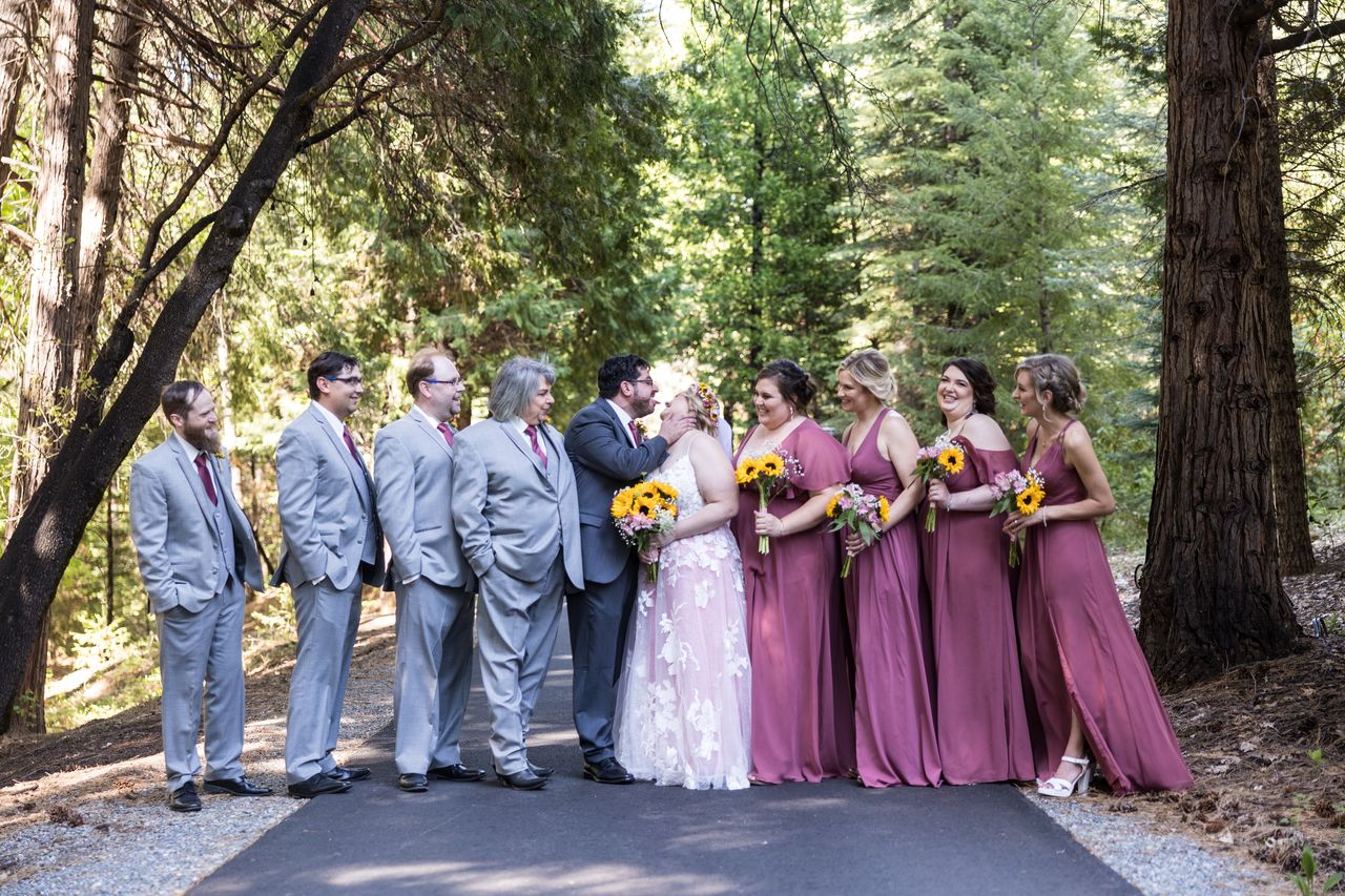 The wedding party lines a forest path while Abney and Chris kiss in the middle