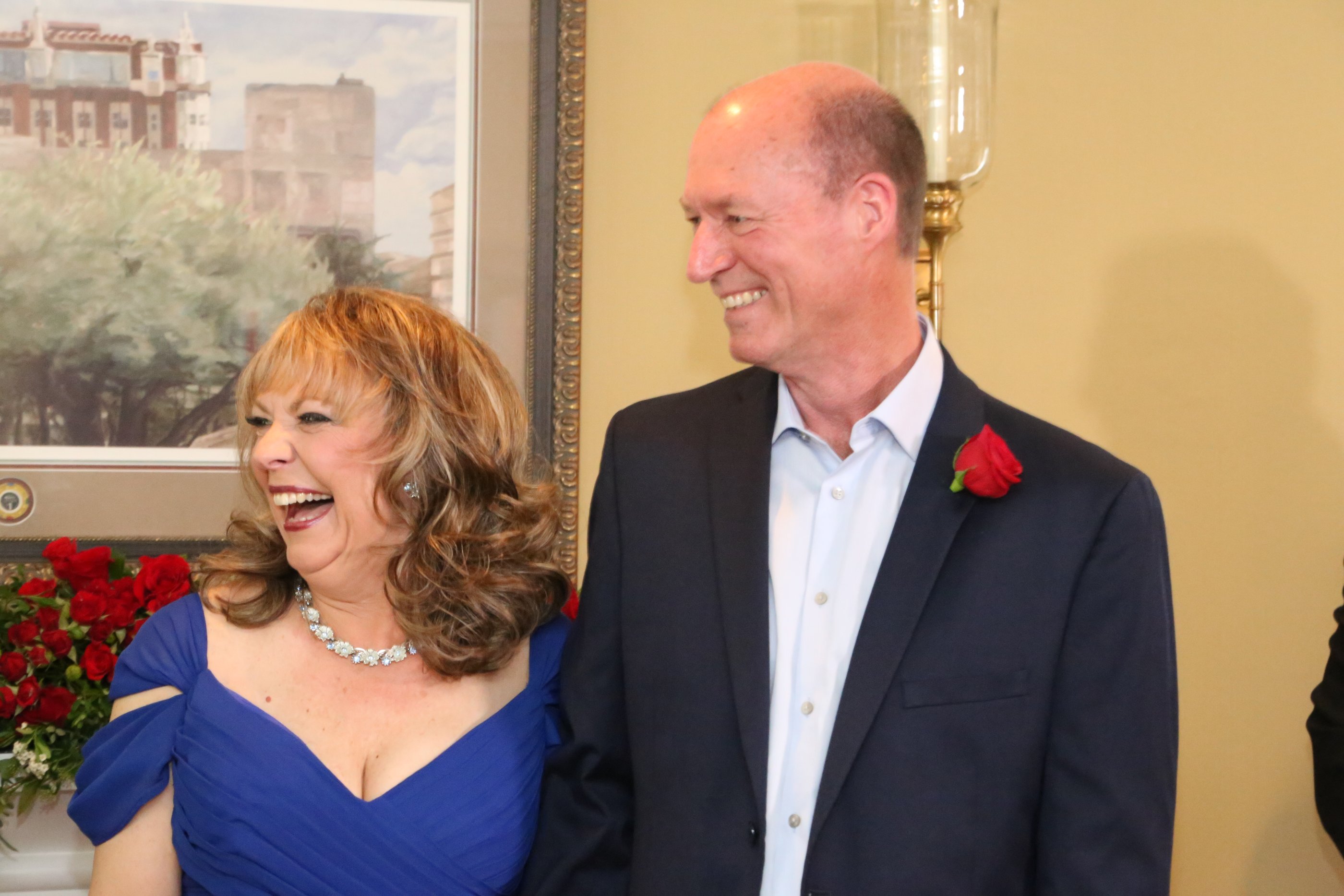 Alexanne laughs beside Tim in front of the rose garland on the mantel during their ceremony